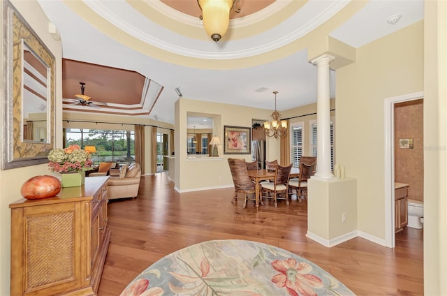 entrance foyer with ceiling fan with notable chandelier, a raised ceiling, crown molding, light wood-type flooring, and decorative columns