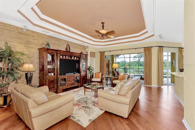 living room with ceiling fan, light hardwood / wood-style floors, a raised ceiling, and ornamental molding