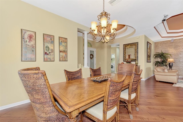 dining area featuring a notable chandelier, decorative columns, crown molding, hardwood / wood-style floors, and a tray ceiling