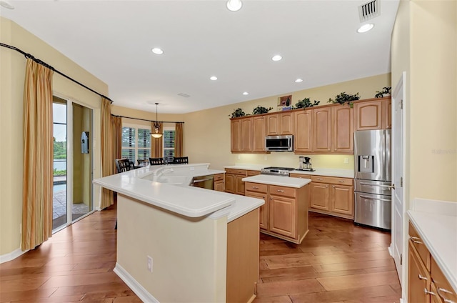 kitchen with a kitchen island, light wood-type flooring, stainless steel appliances, and hanging light fixtures