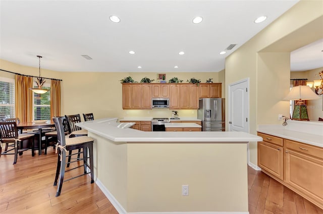 kitchen featuring hanging light fixtures, stainless steel appliances, a breakfast bar area, a kitchen island, and light wood-type flooring