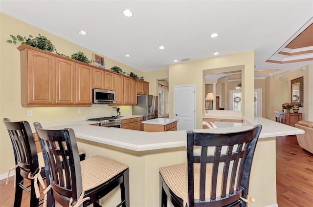 kitchen featuring kitchen peninsula, appliances with stainless steel finishes, ornamental molding, a breakfast bar, and light hardwood / wood-style floors