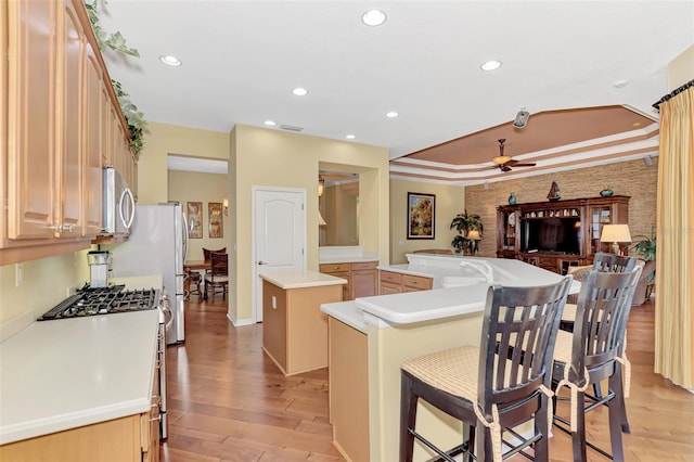 kitchen featuring stainless steel gas range oven, a center island, ceiling fan, a kitchen bar, and kitchen peninsula