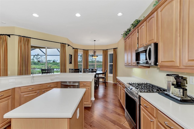 kitchen with light brown cabinets, stainless steel appliances, pendant lighting, a kitchen island, and hardwood / wood-style flooring