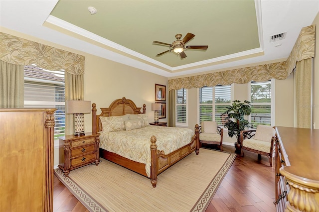 bedroom with hardwood / wood-style flooring, ceiling fan, crown molding, and a tray ceiling