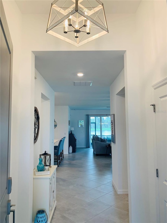 corridor featuring an inviting chandelier and light tile floors