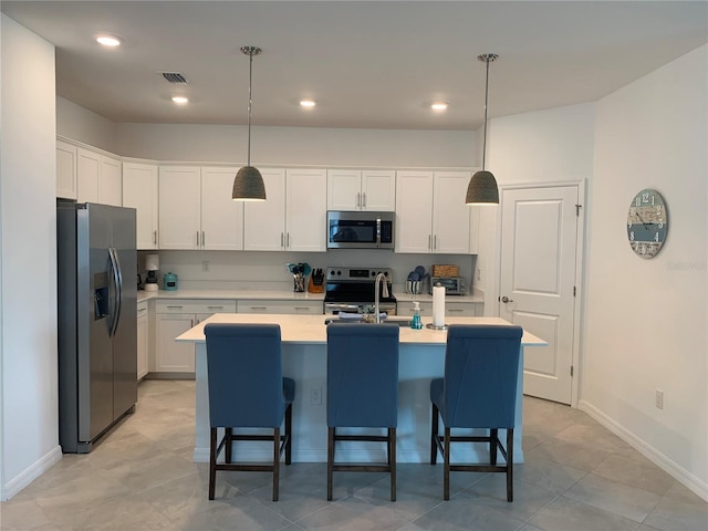 kitchen with a breakfast bar area, stainless steel appliances, an island with sink, white cabinetry, and pendant lighting