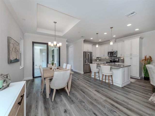 dining area with a notable chandelier, hardwood / wood-style flooring, a tray ceiling, and crown molding