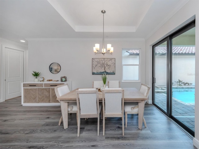 dining area featuring ornamental molding, an inviting chandelier, wood-type flooring, and a raised ceiling