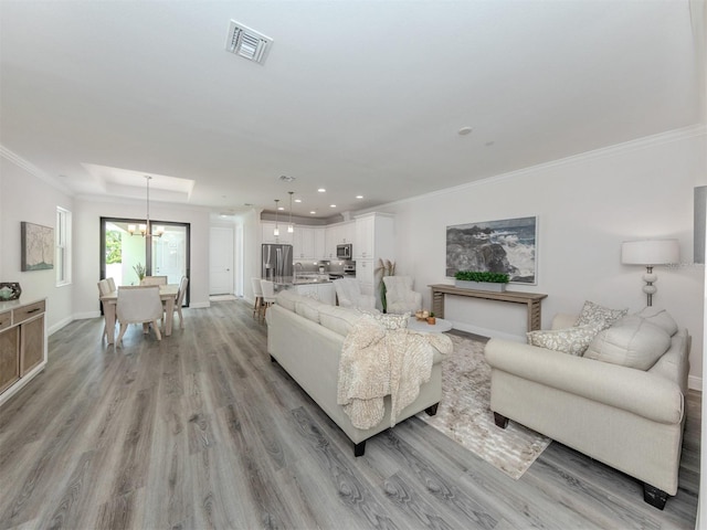 living room featuring sink, light hardwood / wood-style flooring, ornamental molding, and a chandelier