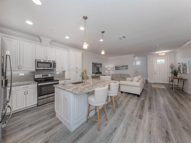 kitchen with light stone counters, stainless steel appliances, light hardwood / wood-style floors, and white cabinets