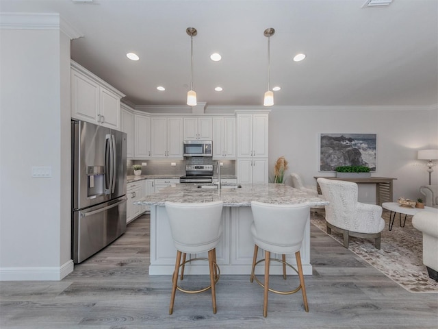 kitchen with hanging light fixtures, light wood-type flooring, a center island with sink, stainless steel appliances, and tasteful backsplash