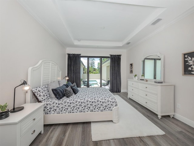 bedroom with hardwood / wood-style floors, ornamental molding, a tray ceiling, and access to exterior