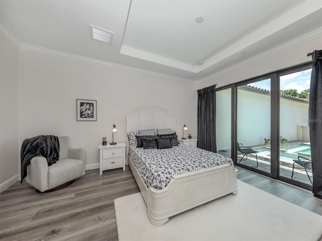 bedroom with hardwood / wood-style floors, ornamental molding, a raised ceiling, and access to outside