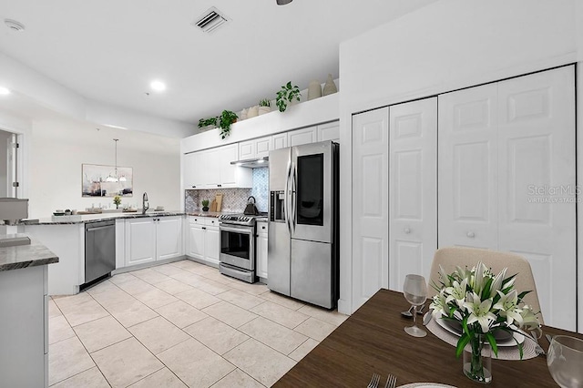 kitchen featuring light tile patterned flooring, kitchen peninsula, white cabinets, backsplash, and appliances with stainless steel finishes