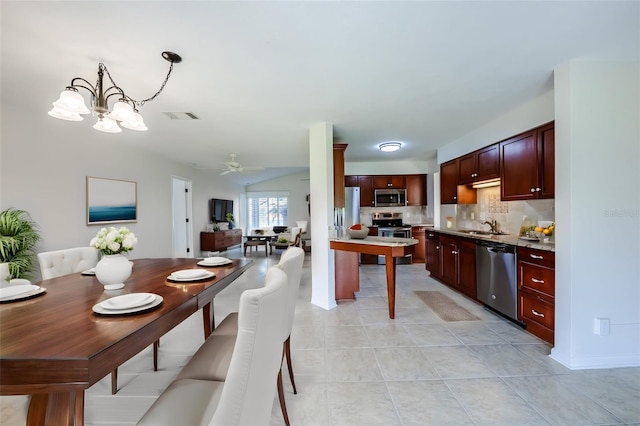 kitchen with stainless steel appliances, light tile floors, ceiling fan with notable chandelier, backsplash, and sink