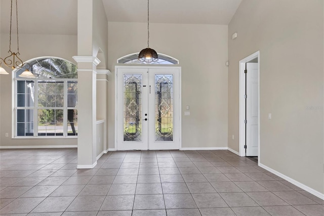 tiled foyer with a towering ceiling, decorative columns, a notable chandelier, and french doors