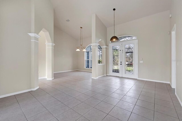 tiled empty room with a chandelier, decorative columns, high vaulted ceiling, and french doors