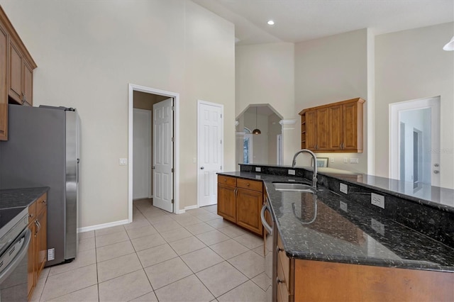 kitchen with a high ceiling, sink, light tile floors, and dark stone counters