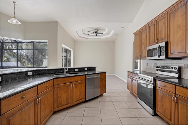 kitchen with ceiling fan, appliances with stainless steel finishes, hanging light fixtures, a raised ceiling, and dark stone countertops