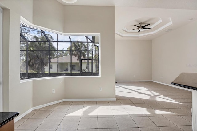 spare room with light tile floors, ceiling fan, and a raised ceiling