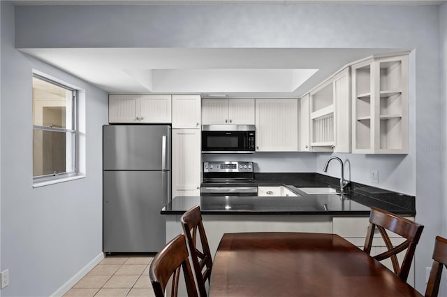 kitchen with sink, light tile floors, stainless steel appliances, a tray ceiling, and white cabinetry