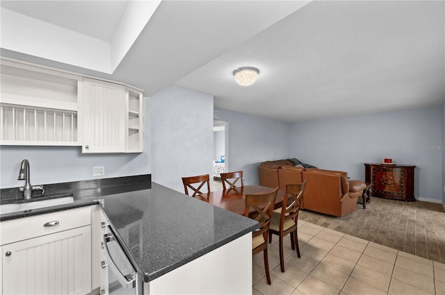 kitchen with kitchen peninsula, white cabinetry, sink, light tile floors, and dark stone countertops