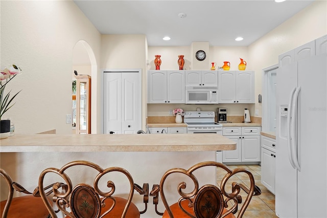 kitchen with white cabinets, light tile floors, a kitchen breakfast bar, and white appliances