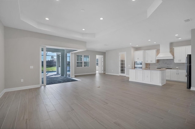 unfurnished living room featuring a raised ceiling and light hardwood / wood-style floors