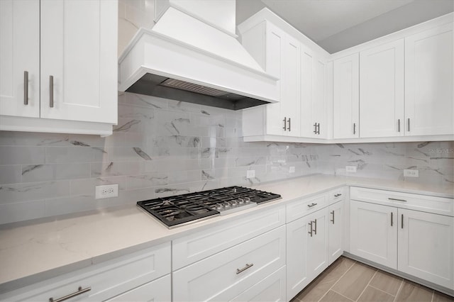 kitchen featuring stainless steel gas cooktop, backsplash, white cabinets, and custom exhaust hood