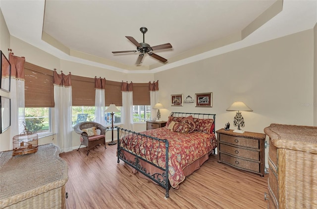 bedroom featuring a tray ceiling, ceiling fan, and light wood-type flooring