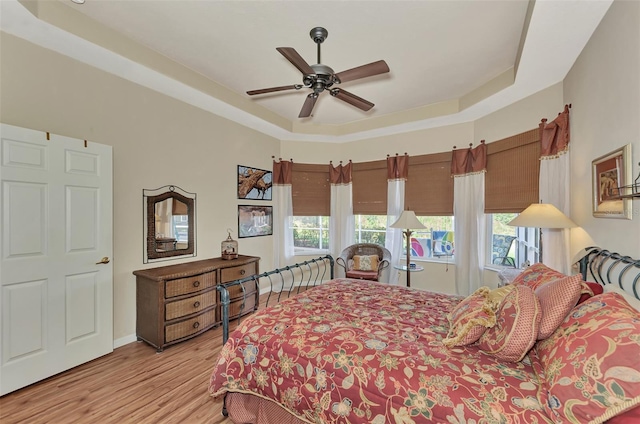 bedroom with a raised ceiling, ceiling fan, and light wood-type flooring