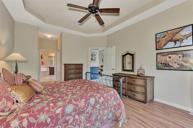 bedroom featuring a raised ceiling, ensuite bathroom, ceiling fan, and light hardwood / wood-style flooring