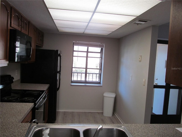 kitchen with light wood-type flooring, a drop ceiling, and black appliances