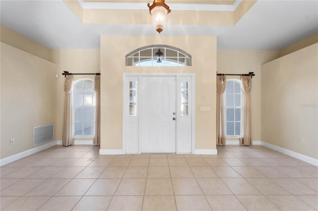 tiled entryway featuring plenty of natural light, a tray ceiling, and ornamental molding