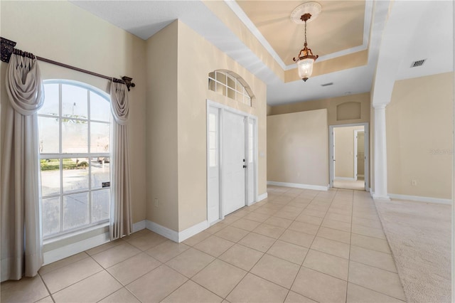 foyer entrance with light carpet, a tray ceiling, and ornate columns