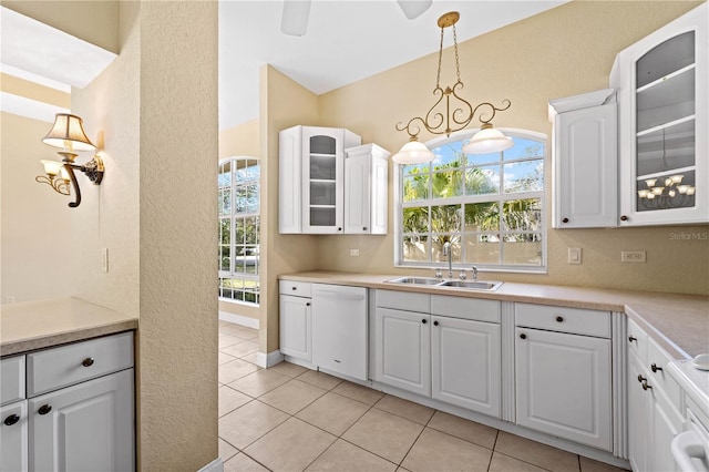 kitchen with sink, white cabinets, dishwasher, light tile flooring, and decorative light fixtures