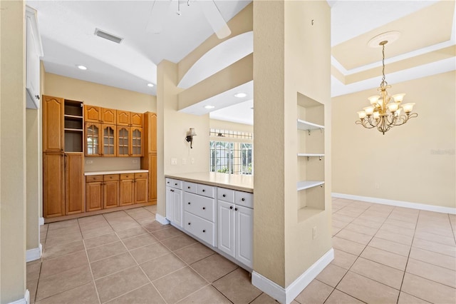 kitchen featuring decorative light fixtures, a tray ceiling, an inviting chandelier, light tile floors, and built in shelves