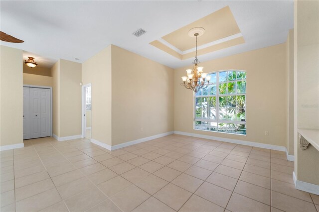 empty room with an inviting chandelier, a raised ceiling, and light tile flooring