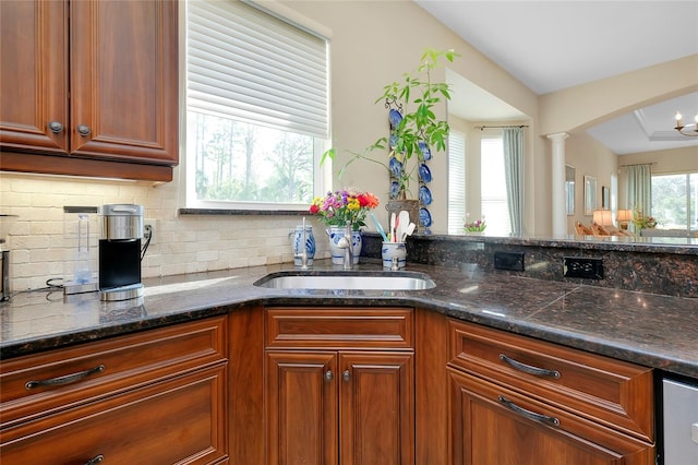 kitchen featuring dark stone counters, decorative backsplash, decorative columns, and sink