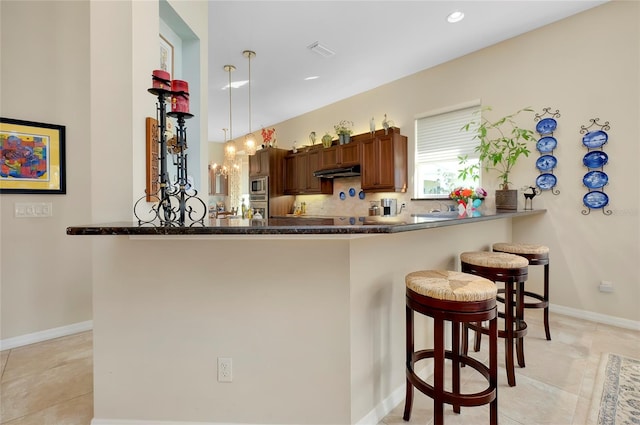 kitchen with kitchen peninsula, decorative light fixtures, a breakfast bar, stainless steel microwave, and decorative backsplash