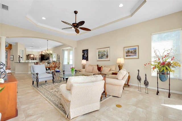 living room with ceiling fan with notable chandelier, crown molding, and a raised ceiling