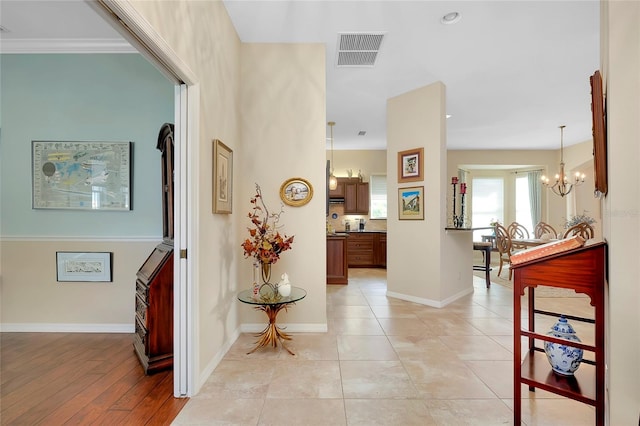 corridor featuring an inviting chandelier, crown molding, and light hardwood / wood-style floors