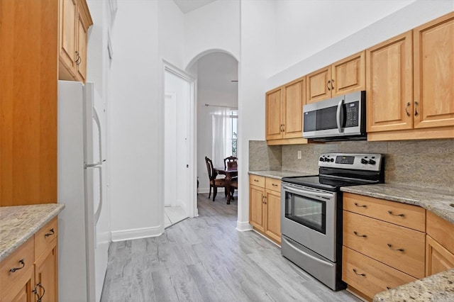 kitchen with backsplash, light hardwood / wood-style floors, stainless steel appliances, and light stone counters