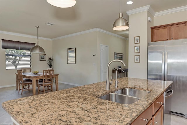 kitchen featuring stainless steel fridge, light stone counters, sink, pendant lighting, and an island with sink