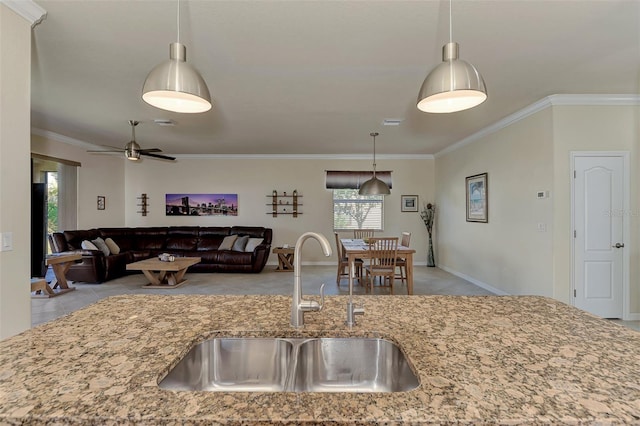 kitchen featuring light stone countertops, ornamental molding, ceiling fan, sink, and hanging light fixtures