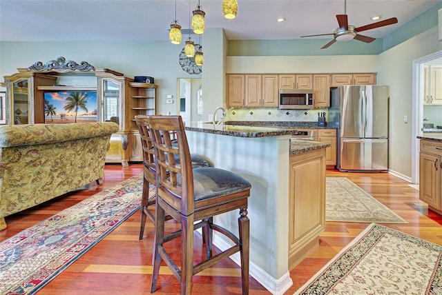 kitchen with ceiling fan, hanging light fixtures, appliances with stainless steel finishes, backsplash, and light wood-type flooring