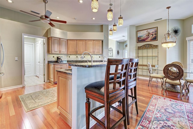 kitchen with ceiling fan, a kitchen bar, light wood-type flooring, dark stone counters, and pendant lighting