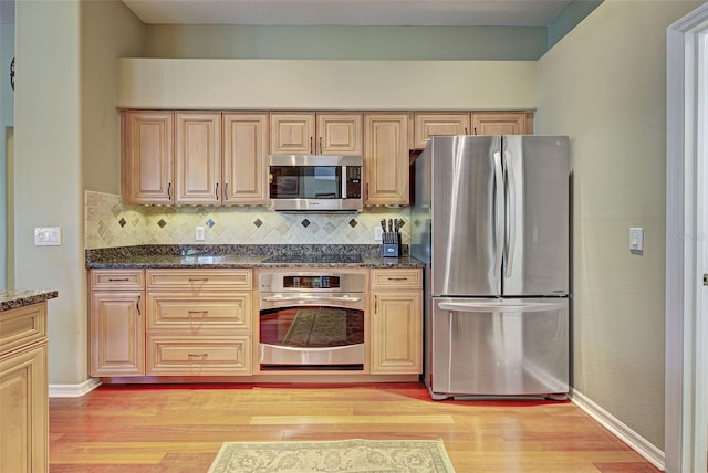 kitchen featuring backsplash, dark stone countertops, light hardwood / wood-style flooring, and appliances with stainless steel finishes