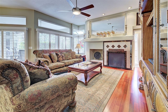 living room with a fireplace, ceiling fan, and light wood-type flooring